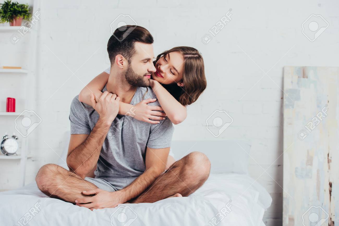 117877809-adult-couple-hugging-and-sitting-on-bed-with-white-bedding